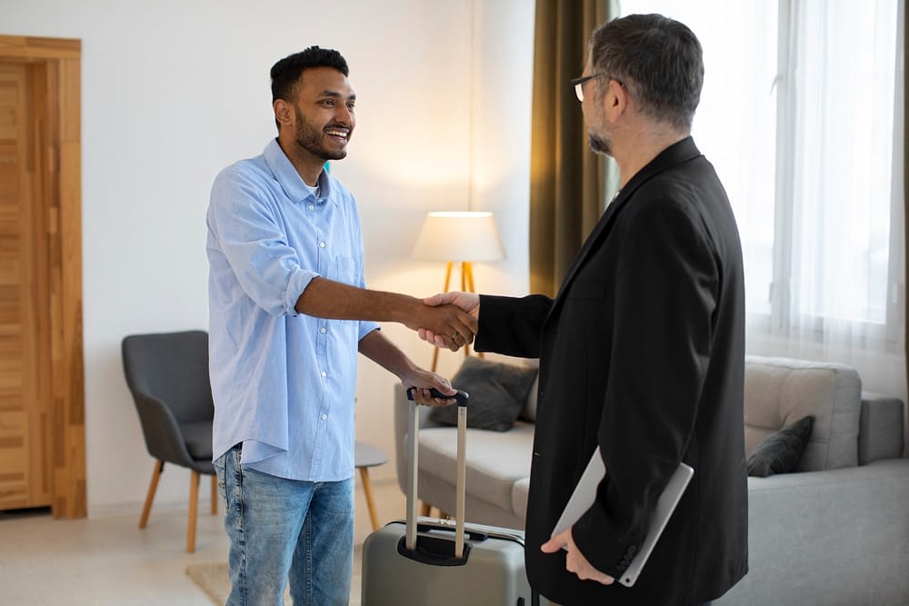 Guest arriving at a furnished apartment in Paris, shaking hands with the host while holding a suitcase